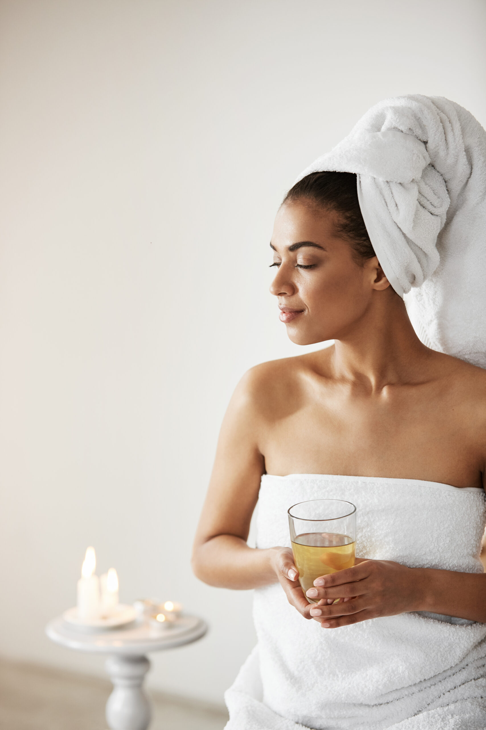 african girl with towel on head holding glass smiling looking in side resting in spa resort.
